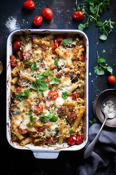 a casserole dish filled with pasta, tomatoes and basil on a dark surface