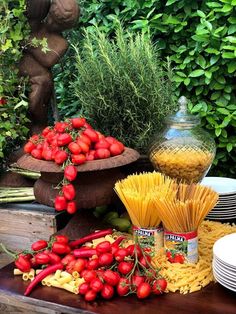 pasta, tomatoes and other vegetables on a table in front of a statue with greenery