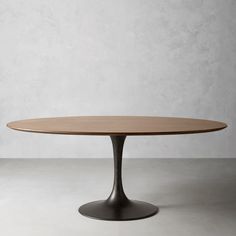 an oval wooden table sitting on top of a white floor next to a gray wall