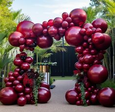 an archway made out of red balloons and greenery in the middle of a garden