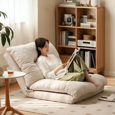 a woman sitting in a chair with a book on her lap, reading a magazine