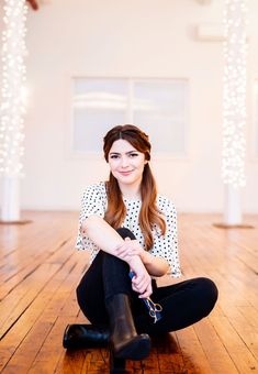 a woman is sitting on the floor with her legs crossed and holding onto a pair of black boots