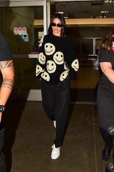 the woman is walking through an airport carrying her luggage and smiling at the camera man