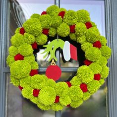 a green wreath with red, white and green pom - poms hanging from it