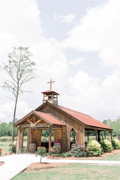 a small wooden church with a cross on the roof and flowers in front of it