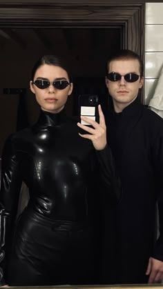 a man and woman in black catsuits taking a selfie