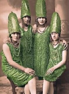 four women in green dresses and hats sitting on a bench