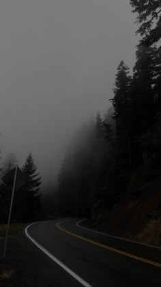 an empty road in the fog with trees on both sides and a street sign next to it