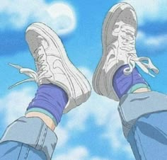 someone's feet with blue jeans and sneakers on, standing in front of the sky