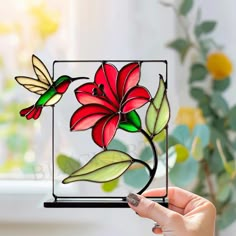 a hand holding up a stained glass piece with red flowers and green leaves on it