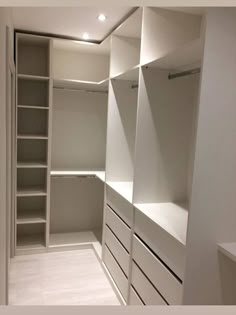 an empty walk in closet with white shelves and drawers on both sides, along with no doors