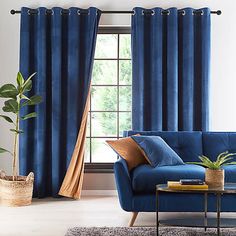 a living room with blue couches and curtains in front of a large window that has a potted plant next to it