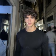 a man in black shirt standing next to a building with people walking by him and looking at the camera