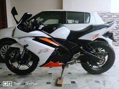 a white and orange motorcycle parked in front of a car on a checkered tile floor