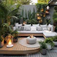 an outdoor living area with lots of plants and candles on the table, surrounded by potted plants