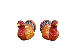 two ceramic turkeys sitting next to each other on a white surface with one red and the other yellow