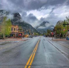 an empty street with mountains in the background and cloudy skies above it on a rainy day