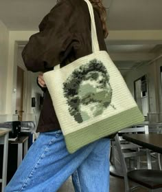 a woman carrying a cross - stitch bag with an image of a man's face on it