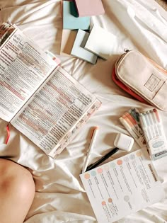 a person laying on top of a bed next to an open book and some pens