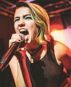 a woman singing into a microphone with her mouth wide open and tongue out, on stage