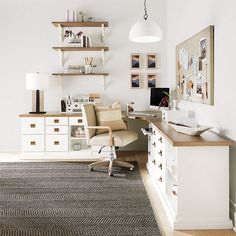 a home office with white walls and wooden flooring is pictured in this image, there are shelves on the wall above the desk