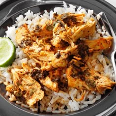 a black plate topped with rice and chicken next to a slice of lime wedged in the middle