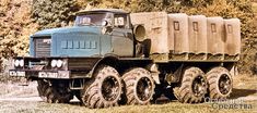 an old truck with large tires is parked in the grass next to some trees and bushes