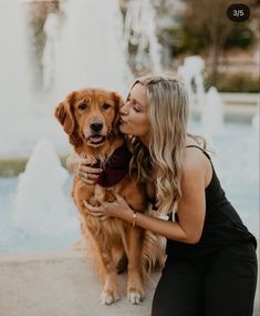 a woman kissing her dog in front of a fountain