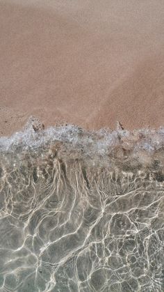 the beach is covered with waves and clear blue water, as seen from above on a sunny day