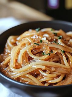 a black bowl filled with pasta and sauce on top of a white cloth covered table