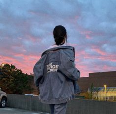 a woman walking across a parking lot under a pink and blue sky with clouds in the background