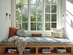 a window seat with pillows and blankets on it in front of a window filled with books