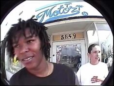 two men are standing in front of a store and one is looking at the camera