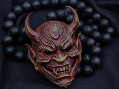 a red demon mask is surrounded by black beads