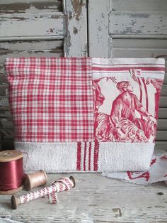 a red and white pillow sitting on top of a table next to spools of thread