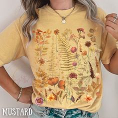 "This botanical shirt with autumn inspired wildflower meadows pressed flowers captures the essence of nature's beauty and makes a splendid addition to your wardrobe. This shirt is not just a wardrobe staple; it's a heartfelt gesture for any occasion. Be it Mother's Day or a spontaneous surprise, it's a thoughtful gift that speaks to her love for all things floral and natural. Elevate her style and express your appreciation with this exquisite wildflower tee, a symbol of beauty, serenity, and the Fall Yellow Shirt With Floral Print, Fall Floral Print T-shirt, Floral Print Crew Neck Shirt For Fall, Fall Floral Print Crew Neck Shirt, Flowery Outfits, Flower Minimalist, Floral Clothing, Wildflower Field, Autumn Inspired