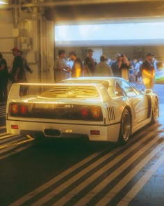 a white car driving down a street next to a group of people in the background