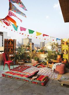 an outdoor area with lots of furniture and decorations on the roof, in front of a cityscape