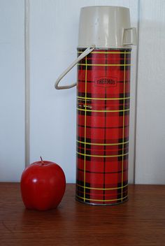 a red apple sitting next to a canister on top of a wooden table in front of a white wall