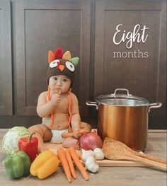 a baby sitting on the floor next to vegetables and a pot with a spoon in it