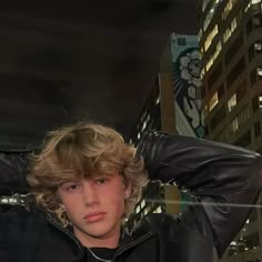 a young man wearing a black leather jacket in front of a cityscape at night