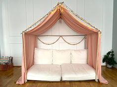 a white couch with pink drapes and pillows on it's sides in front of a wooden floor