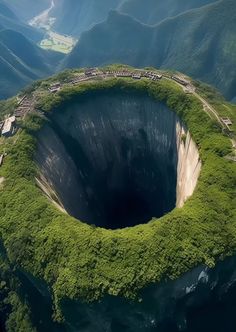 an aerial view of a large crater in the middle of some mountains with trees growing around it