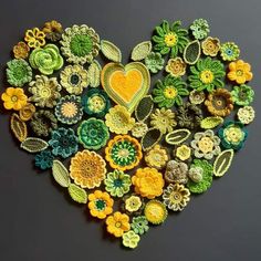 a heart made out of crocheted flowers on a black surface with green and yellow colors