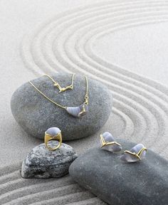 two pieces of jewelry sitting on top of a rock next to some rocks and sand