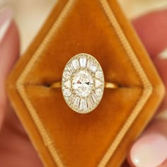 a close up of a person holding a ring in front of a box with a diamond on it