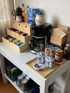 a coffee maker sitting on top of a white table next to some cups and containers