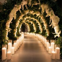 rows of candles lined up in front of an archway with flowers and greenery on either side