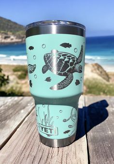 a blue tumbler cup sitting on top of a wooden table next to the ocean