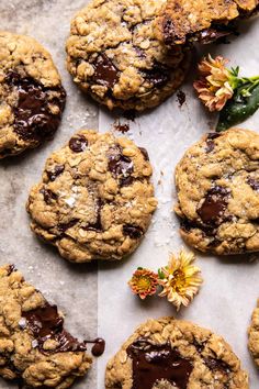 chocolate chip cookies are arranged on a sheet of parchment paper with dried flowers and leaves